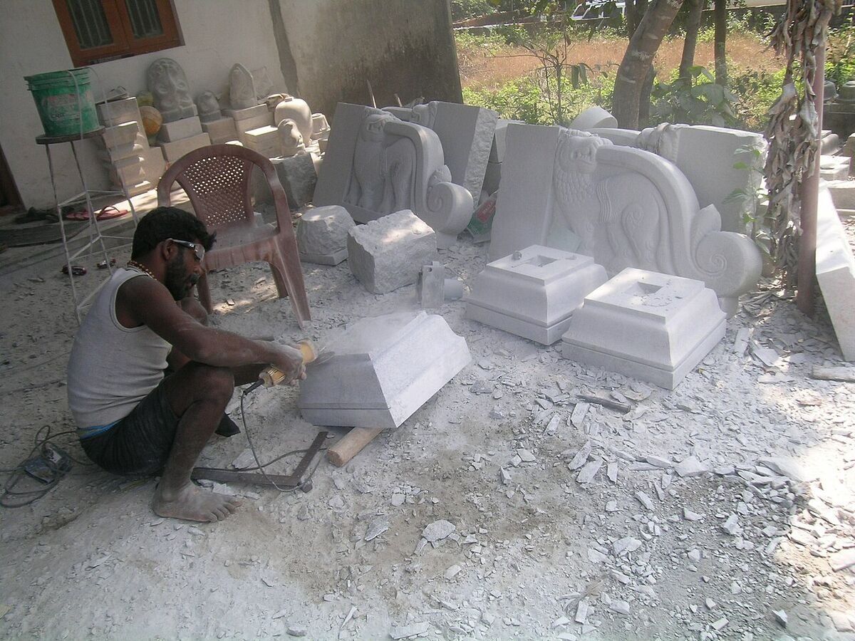 A stone carver at work in Sanoor, Karkala, shaping a granite block, with finished carved lion brackets and pedestals behind him